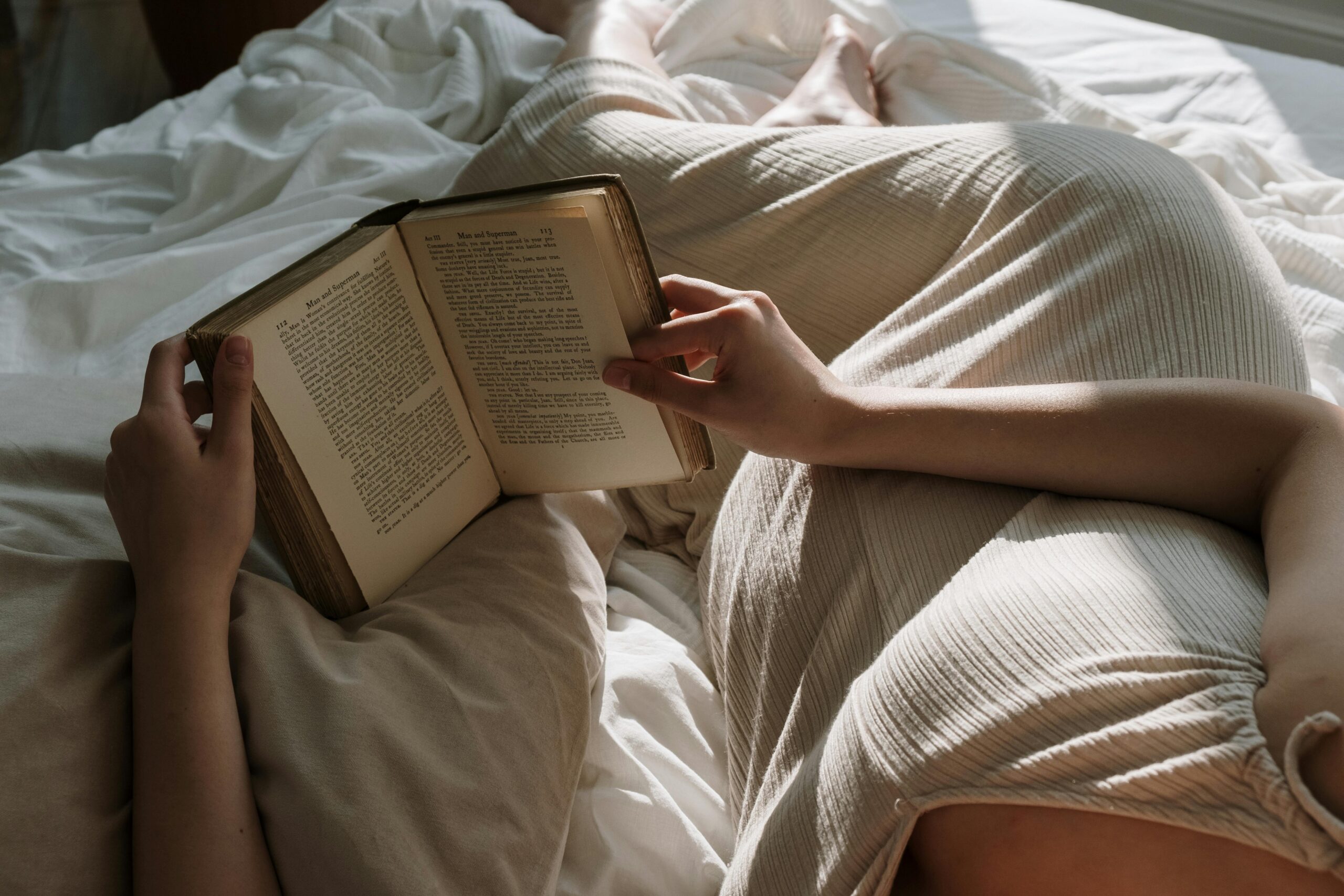 Mulher deitada na cama lendo um livro em um momento de descanso e autocuidado.