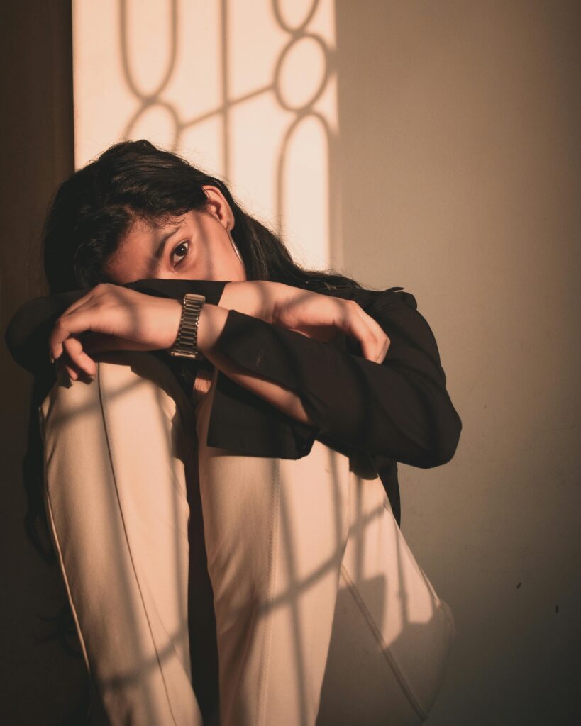 Mulher sentada apoiando os braços nos joelhos, com expressão cansada e olhar distante, ilustrando sinais de cansaço mental em um ambiente iluminado pelo sol.