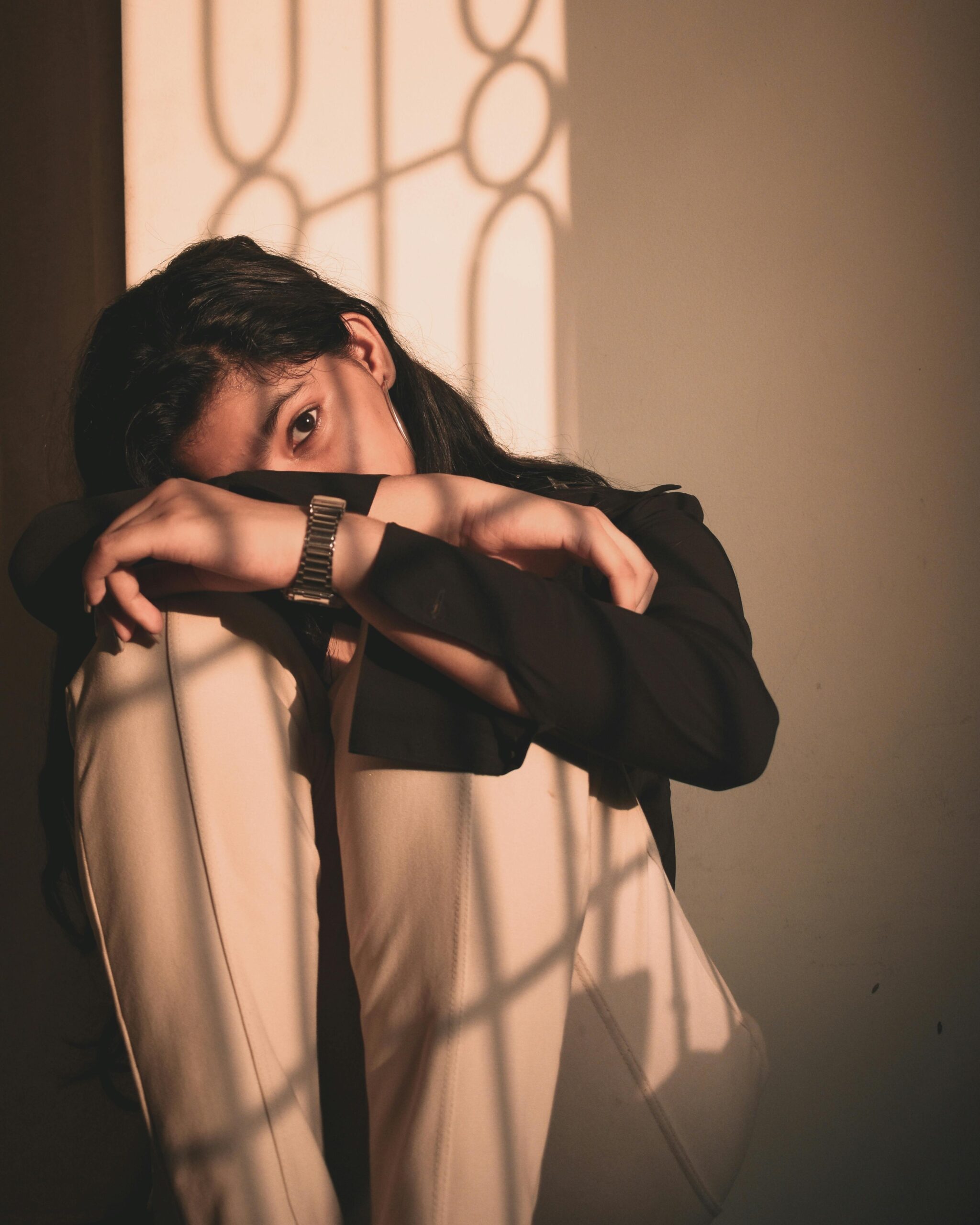 Mulher sentada apoiando os braços nos joelhos, com expressão cansada e olhar distante, ilustrando sinais de cansaço mental em um ambiente iluminado pelo sol.