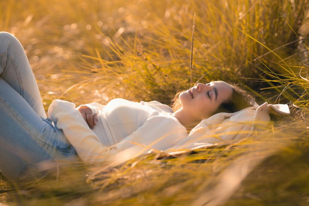 Mulher deitada na natureza com expressão de tranquilidade, simbolizando descanso, equilíbrio emocional e práticas conscientes para elevar a vibração.