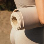 Pessoa segurando um tapete de yoga ao ar livre, representando hábitos de autocuidado, movimento consciente e a construção de uma rotina saudável.