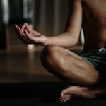 Um homem sem camisa em um estúdio de ioga praticando meditação na posição de lótus para relaxamento e bem-estar.