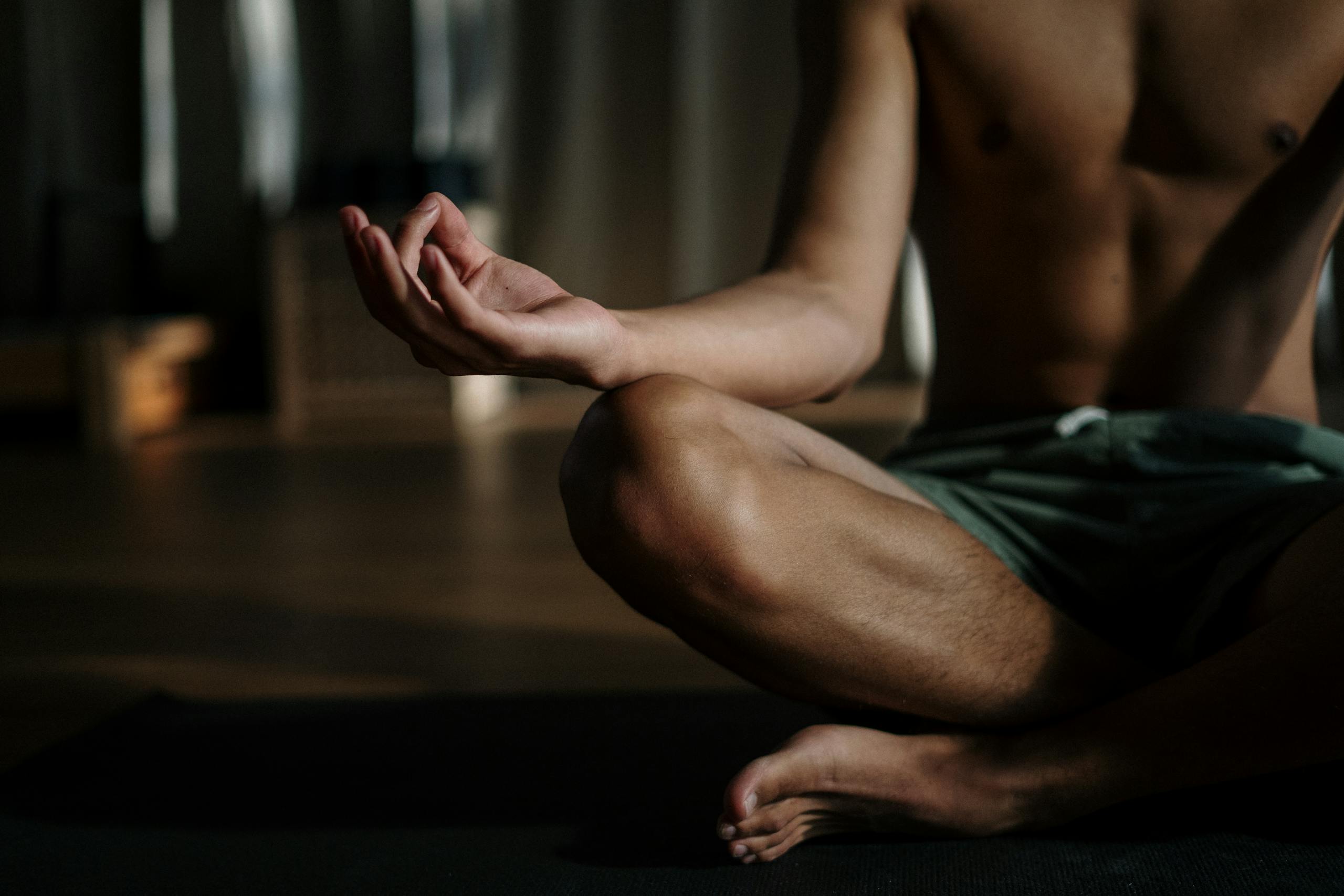 Um homem sem camisa em um estúdio de ioga praticando meditação na posição de lótus para relaxamento e bem-estar.